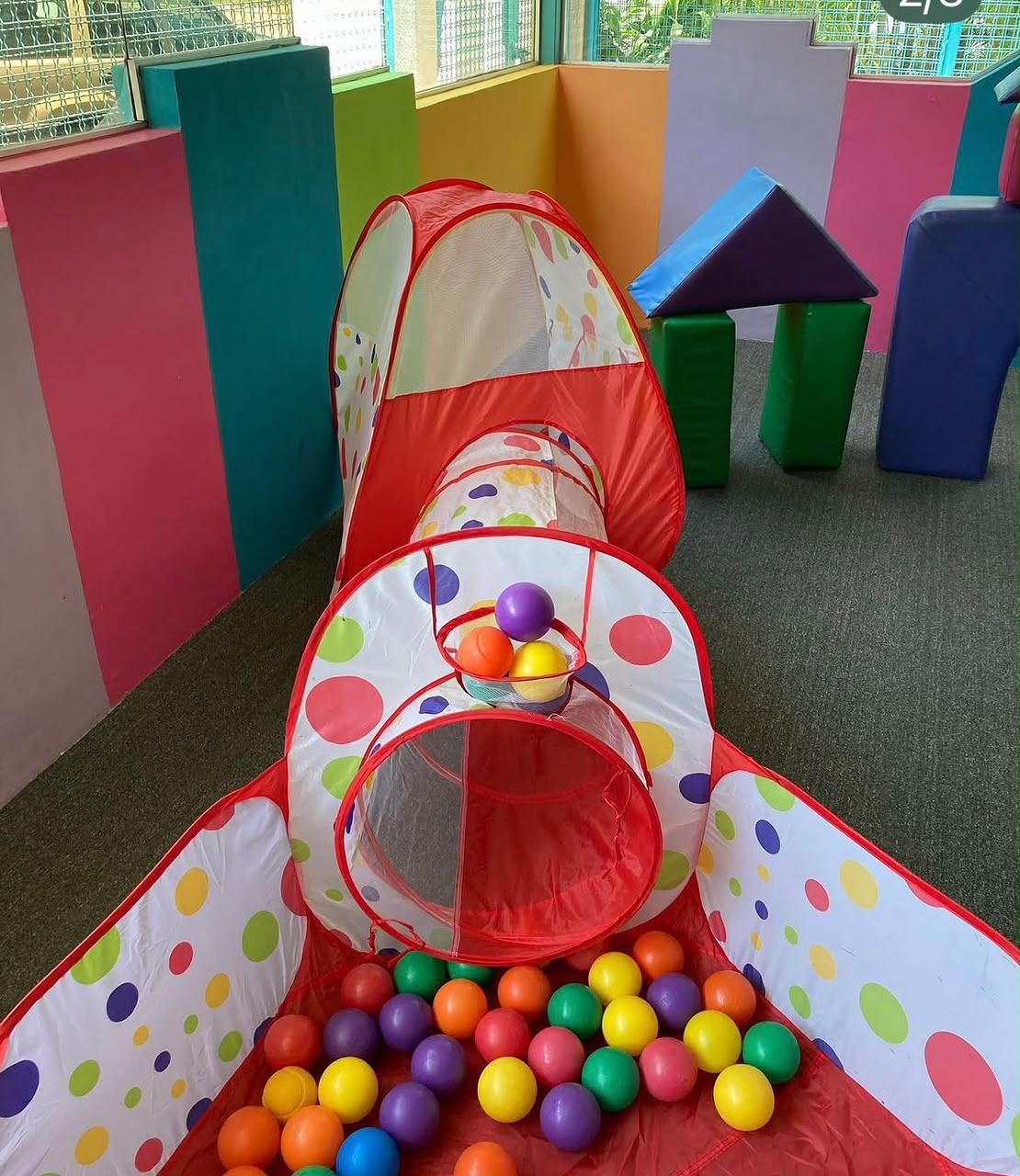 Área psicomotriz con túnel de tela, piscina de pelotas y módulos de goma espuma