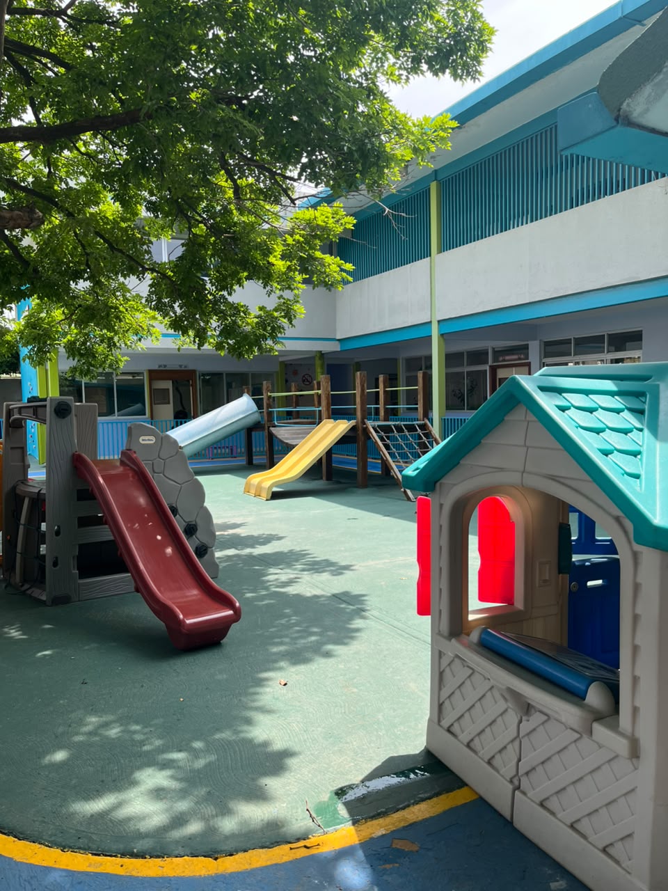 Parque con toboganes, puente colgante y red de trepar frente al edificio del preescolar