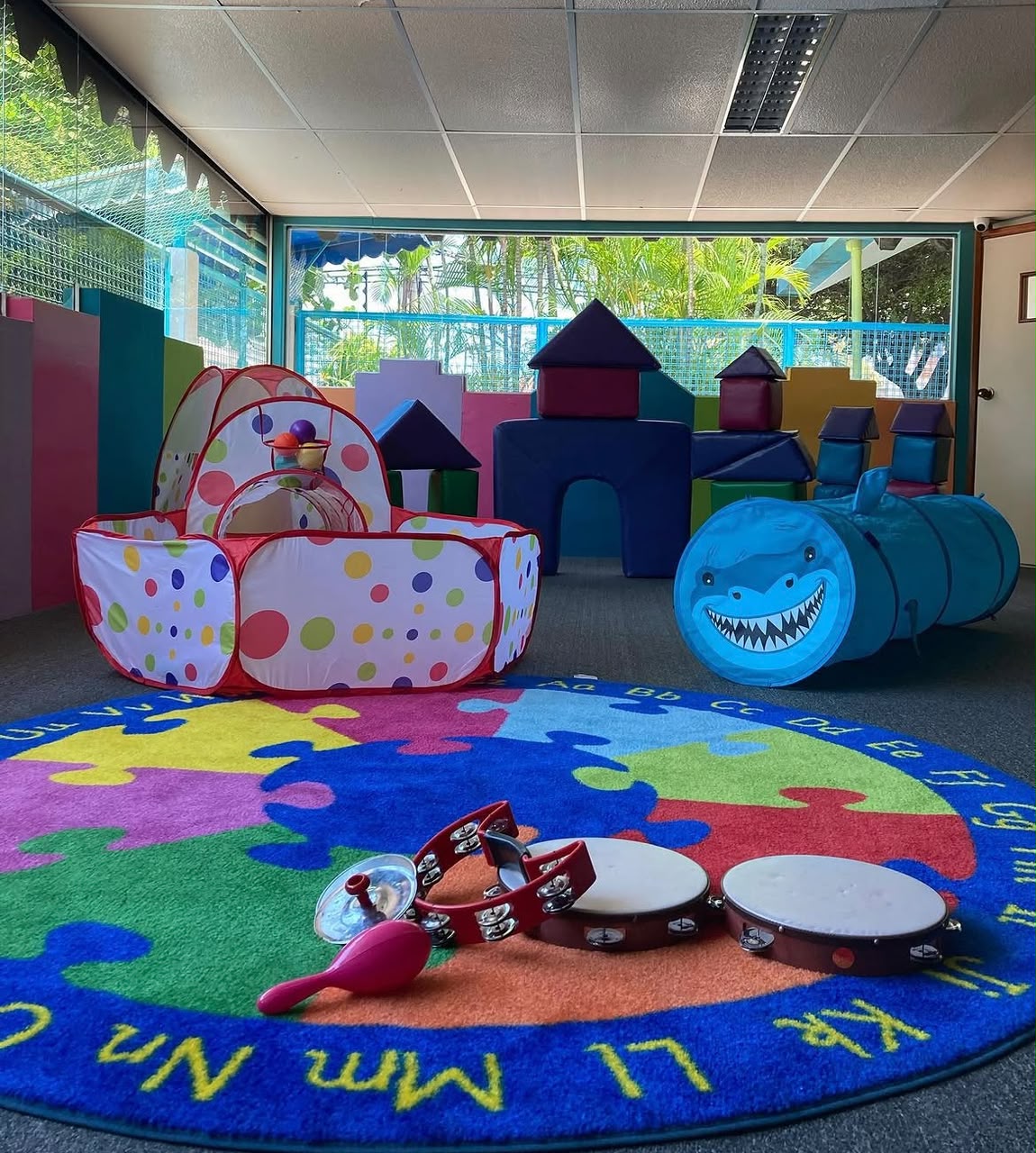 Salón de juegos de The Preschool con alfombra del abecedario, bloques suaves e instrumentos musicales